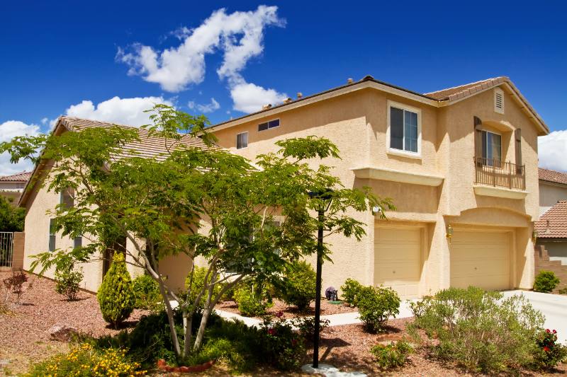 Tan two-story house with two-car garage, landscaped front yard, blue sky