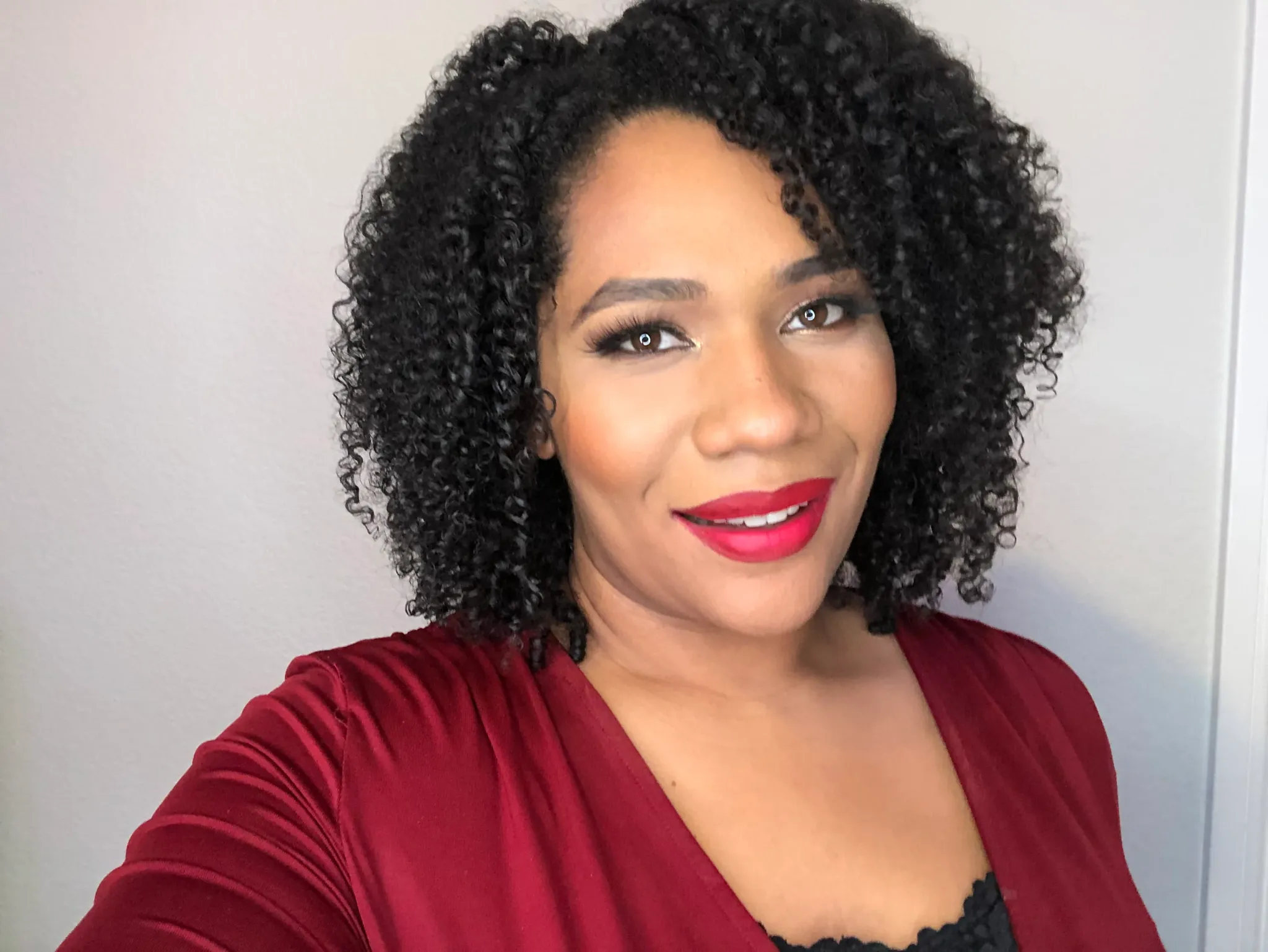 Professional headshot of woman with curly black hair wearing burgundy cardigan and red lipstick